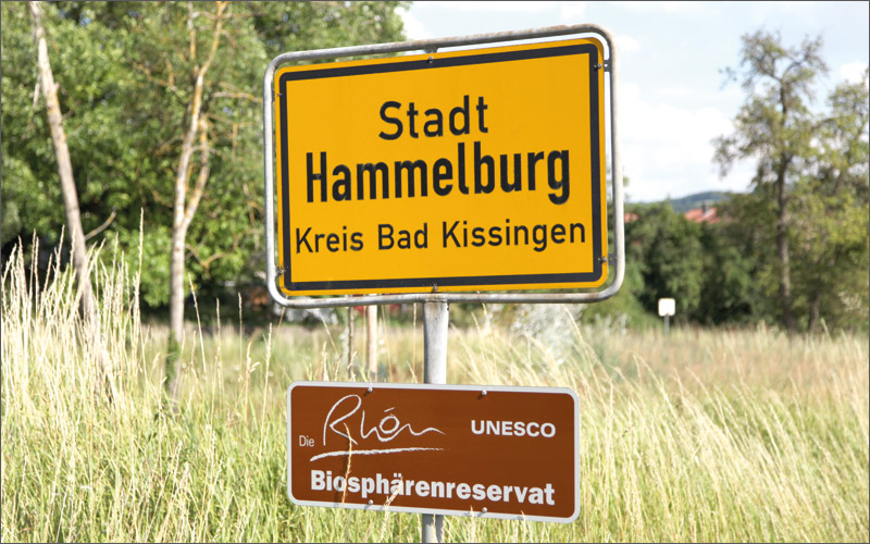 Ortsschild von Hammelburg mit Landschaft im Hintergrund