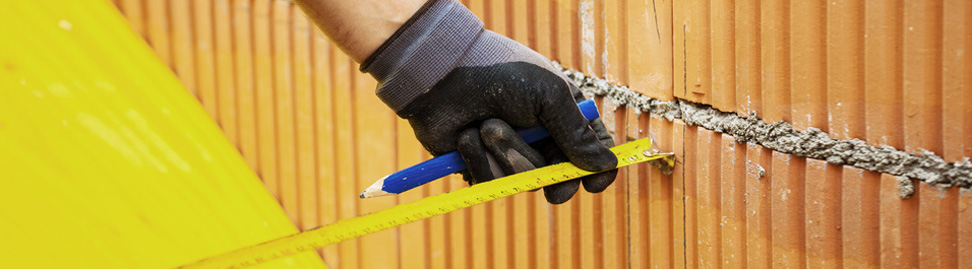 Hand hält Maßband und Stift in der Hand, Backsteinmauer